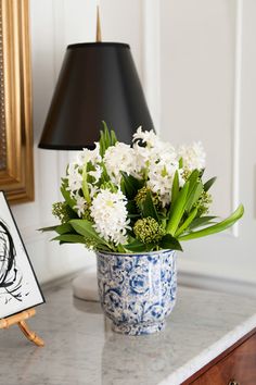 a blue and white vase filled with flowers next to a lamp on top of a table