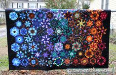 a colorful quilt is hanging on a fence in front of a house with trees and grass