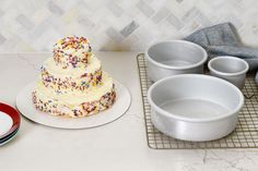 a cake with sprinkles sits on a table next to bowls and plates