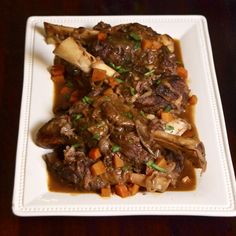 a white plate topped with meat and veggies covered in gravy on top of a wooden table