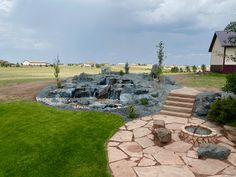 a stone patio and fire pit in the middle of a grassy area with steps leading up to it