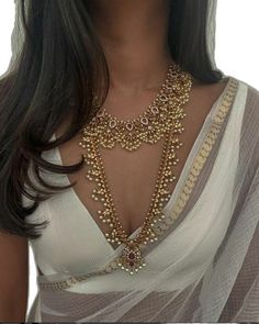 a woman wearing a white top and gold necklace with beads on her chest, standing in front of a white background