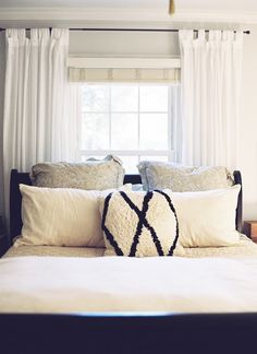 a bed with white sheets and pillows in front of a window