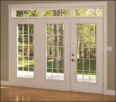 an empty room with french doors and windows on the outside, in front of some trees