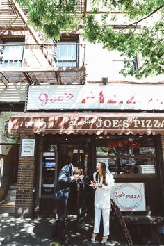 a man and woman standing in front of a pizza shop