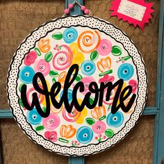 a welcome sign hanging on the side of a blue door with pink, yellow and green flowers