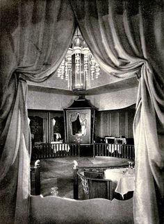 an old black and white photo of a living room with drapes on the windows