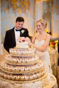 the bride and groom are cutting their wedding cake at the reception table with cupcakes in front of them