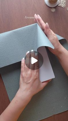 a woman is cutting out a piece of paper on top of a wooden table next to a cup of coffee