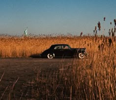 an old car is parked in the middle of a field with tall grass and a statue