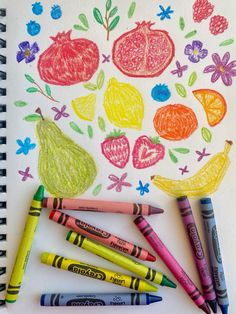 some crayons are laying on top of a paper with fruit and flowers drawn on it