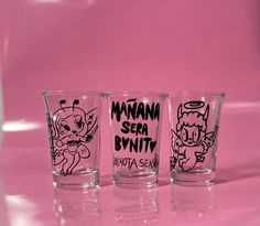 three shot glasses sitting on top of a pink surface with cartoon characters painted on them