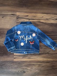 a denim jacket with butterflies and the word may on it, sitting on top of a wooden floor