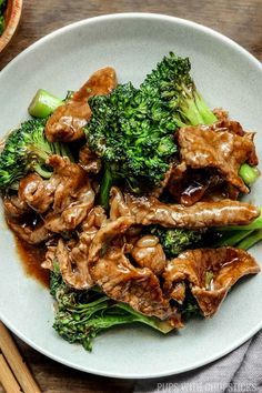 beef and broccoli on a white plate with chopsticks next to it