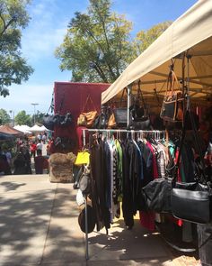 an outdoor market with clothes and handbags hanging from the rack, on a sunny day