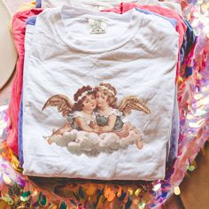 Get ready to show your style with our Vintage Angel Distressed T-Shirt! Perfect for a beach party, concert or or just a casual day out, this graphic tee is a must-have.  Proudly Printed on Comfort Colors® tees, for that insanely soft, vintage look and feel.  Without doubt, this will be your favorite shirt. With its vintage-inspired design, this shirt is perfect for those who love a boho, western, or retro look. The oversized fit and soft, comfortable fabric make it the perfect choice for a day o Cherub Aesthetic Clothes, Angel Shirt Aesthetic, Pink Angel Top, Brandy Melville Cherub Top, Angel T Shirt, Angel Core, Vintage Angel, Aesthetic T Shirts, Comfort Colors Tee