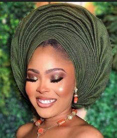 a woman wearing a green head wrap with orange beads on her necklace and gold eyeshadow