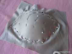 a white piece of cloth with pins and thread on it sitting on a pink surface