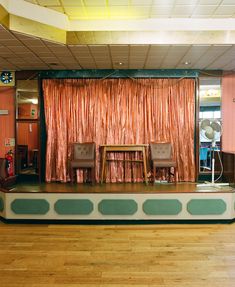 an empty stage with chairs and a table in front of a curtained area on the floor