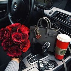 a bouquet of red roses sitting on top of a car dashboard next to a cup of coffee