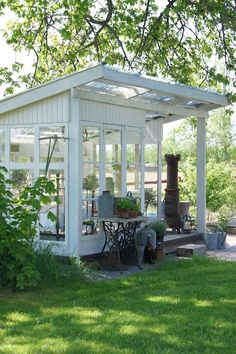 a small white shed sitting in the middle of a lush green field