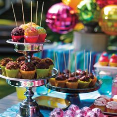 cupcakes and muffins are displayed on three tiered trays with candy sticks sticking out of them