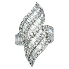 Ring size: 7.5 This lustrous, sparkling cocktail ring is a captivating embodiment of modern artistry and timeless luxury. Crafted in shimmering 14 karat white gold, its design is a marvel, resembling fiery flames that dance with movement. This distinctive ornament is adorned with a mesmerizing array of baguette and round diamonds, which, in unison, create an intricate play of light and shadow. The elegant piece absolutely glows, drawing all eyes to the hand and flattering the finger with its elongated silhouette. The diamonds, both round and baguette-cut, continue their scintillating journey along the shank of the ring, ensuring that elegant shimmer and sparkle grace every facet of this opulent creation. The high polish of the white gold adds more reflective glimmer to this piece, further Sparkling Cocktail, Timeless Luxury, Fine Jewelry Collection, Brilliant Diamond, Ring Size 7, All About Eyes, Cocktail Ring, Diamond Clarity, Light And Shadow