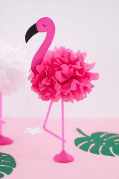 a pink flamingo standing next to a white pom - pom on top of a table