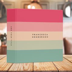 a pink, blue and green book sitting on top of a wooden table next to a lamp