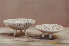 two white ceramic bowls sitting on top of a wooden table next to each other with holes in them