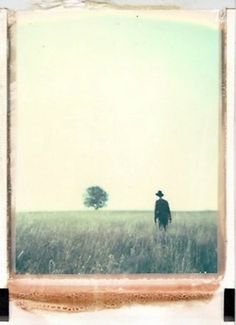 an old photo of a man standing in a field with a lone tree behind him