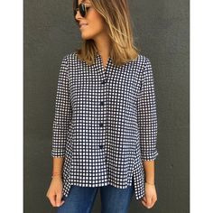 a woman standing in front of a wall wearing jeans and a black and white checkered shirt