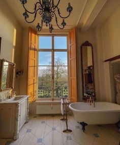 a bathroom with a tub, chandelier and large window overlooking the trees outside