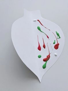 a piece of white paper with red and green paint splattered on it's side