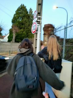 two people walking down the street with their back to each other, one carrying a backpack