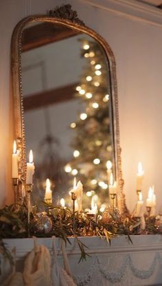 a mantle with candles and a christmas tree in front of a mirror on the wall