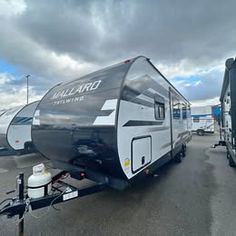 an rv parked in a parking lot next to other vehicles and trailers with cloudy skies