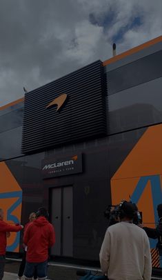 several people standing in front of an orange and black building