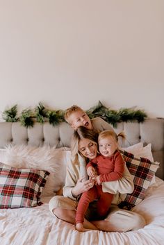 a woman and two children are sitting on a bed with christmas decorations in the background