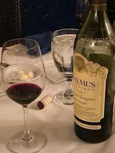 a bottle of wine sitting next to two glasses on a white tablecloth covered table