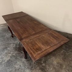 a large wooden table sitting on top of a cement floor next to a white wall