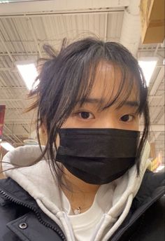 a person wearing a black face mask in a store with long hair and bangs, looking at the camera