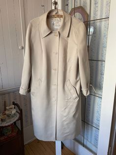 This lovely light beige raincoat was made by London Fog. It fastens with the original buttons in the front, has two front pockets and ties at the cuffs, and is fully lined with off white silky lining. The measurements, taken with the coat lying flat, are: shoulder to shoulder, 18 inches; armpit to armpit, 21 1/2 inches; sleeves, 24 inches; length, 44 inches; bottom edge, 36 inches. In very good condition. Spring Cream Outerwear With Covered Buttons, Classic Beige Raincoat For Fall, Classic Solid Raincoat With Button Closure, Classic Cream Outerwear For Daywear, Vintage Beige Outerwear For Daywear, Classic Beige Raincoat For Winter, Classic Long Beige Raincoat, Classic Beige Winter Raincoat, Classic Beige Long Raincoat