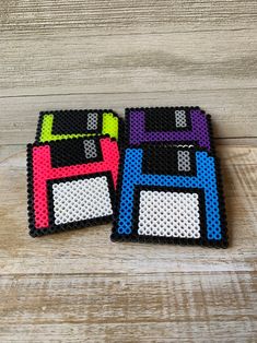 two coasters made out of perler beads are sitting on a wooden surface, one is black and the other is multicolored