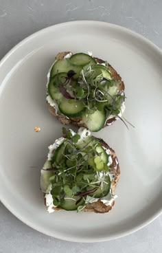 two pieces of bread with cucumbers and cheese on them sitting on a white plate