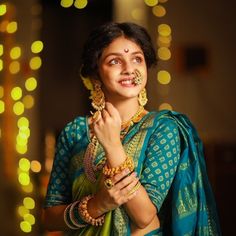 a woman in a blue and green sari with gold jewelry on her neck, smiling at the camera