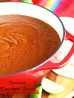 a red pot filled with sauce sitting on top of a wooden cutting board next to sliced limes