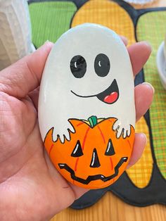 a hand holding a painted rock with a ghost on it and a pumpkin in the middle