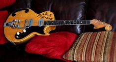 a yellow guitar sitting on top of a brown couch next to a red and white pillow