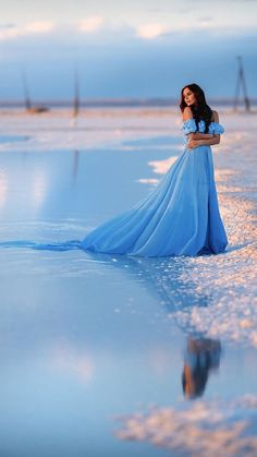 a woman in a blue dress is standing in the water with her hands on her hips